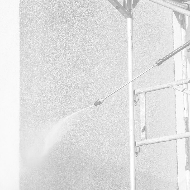 Wasserstrahl eines Hochdruckreinigers trifft eine Außenwand neben einem Gerüst.