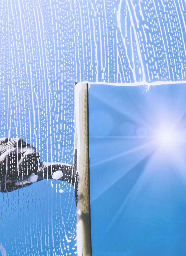Fensterreinigung & Glasreinigung – streifenfrei Fensterabzieher entfernt Seifenwasser von einer Glasscheibe vor blauem Himmel.