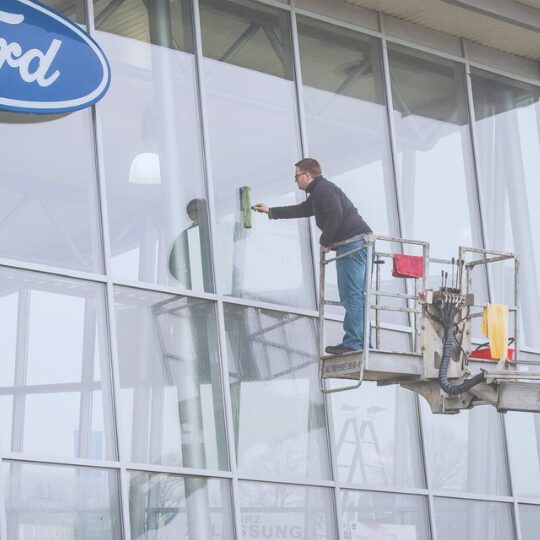 Glasreinigung aussen – Tip-Top Reinigung Mitarbeiter reinigt Glasfassade mit Hubarbeitsbuehne – professionelle Glasreinigung fuer Unternehmen.