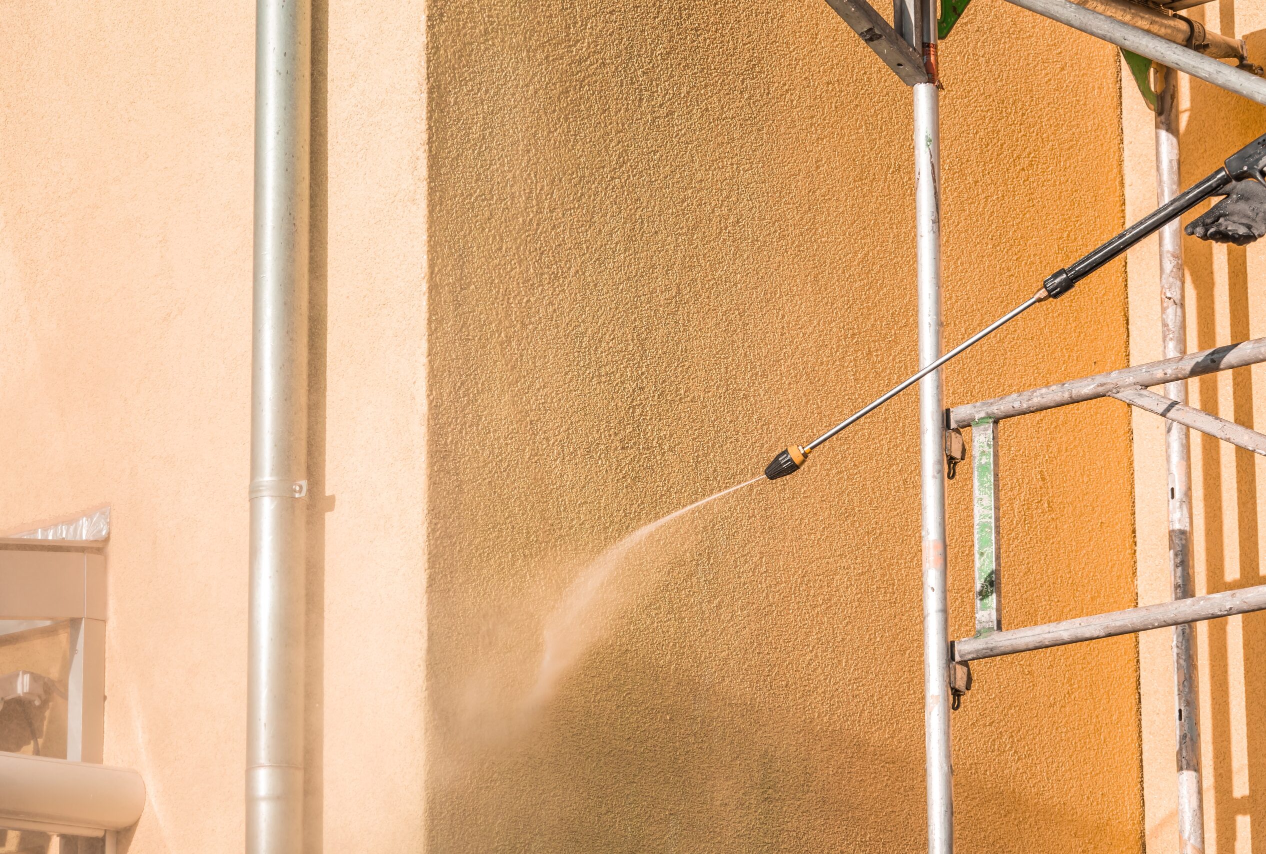 Hochdruckreiniger reinigt Gebaeudefassade am Geruest – Fassadenreinigung fuer sauberen Aussenauftritt.