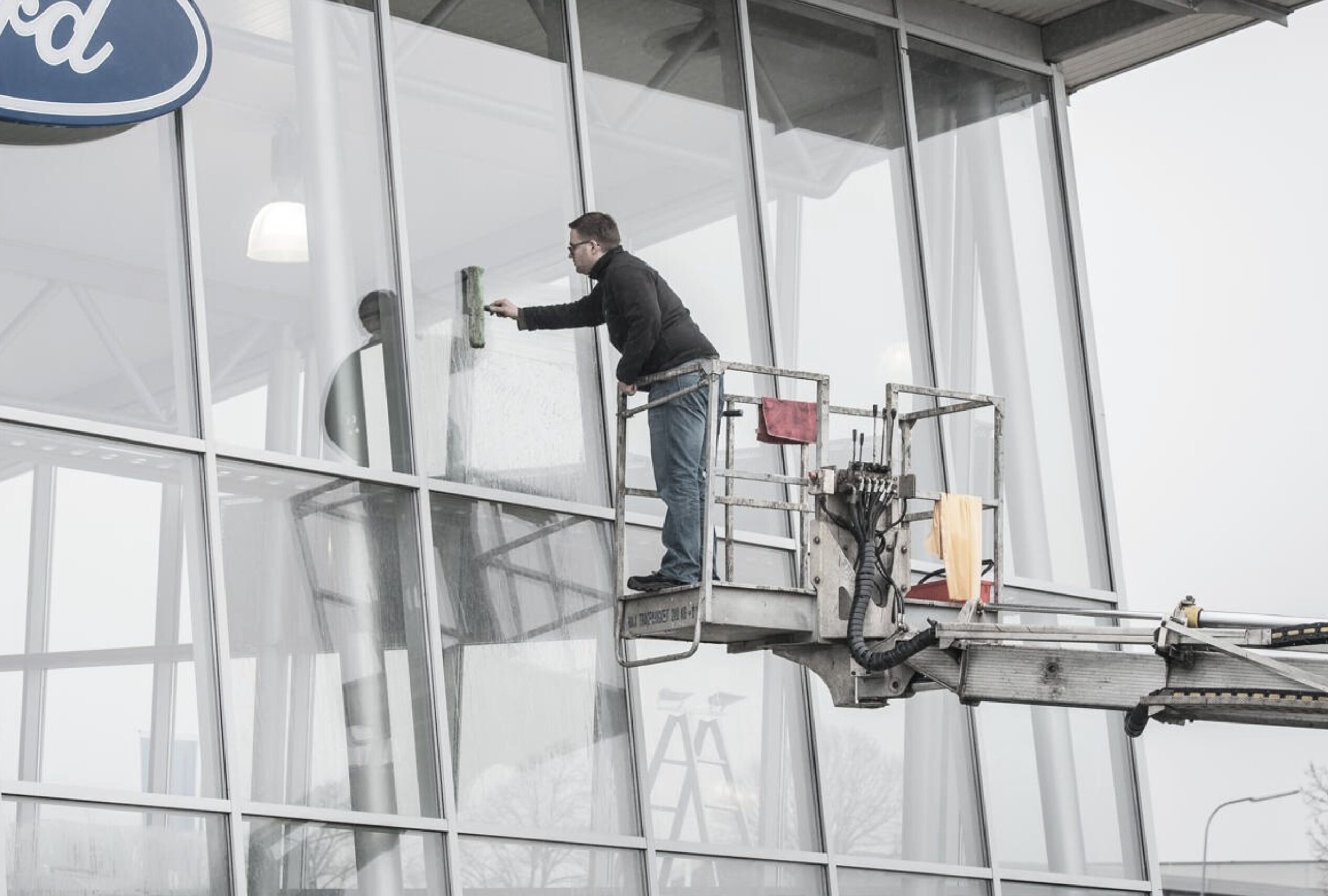 Mitarbeiter reinigt Glasfassade mit Abzieher auf einem Hubsteiger.