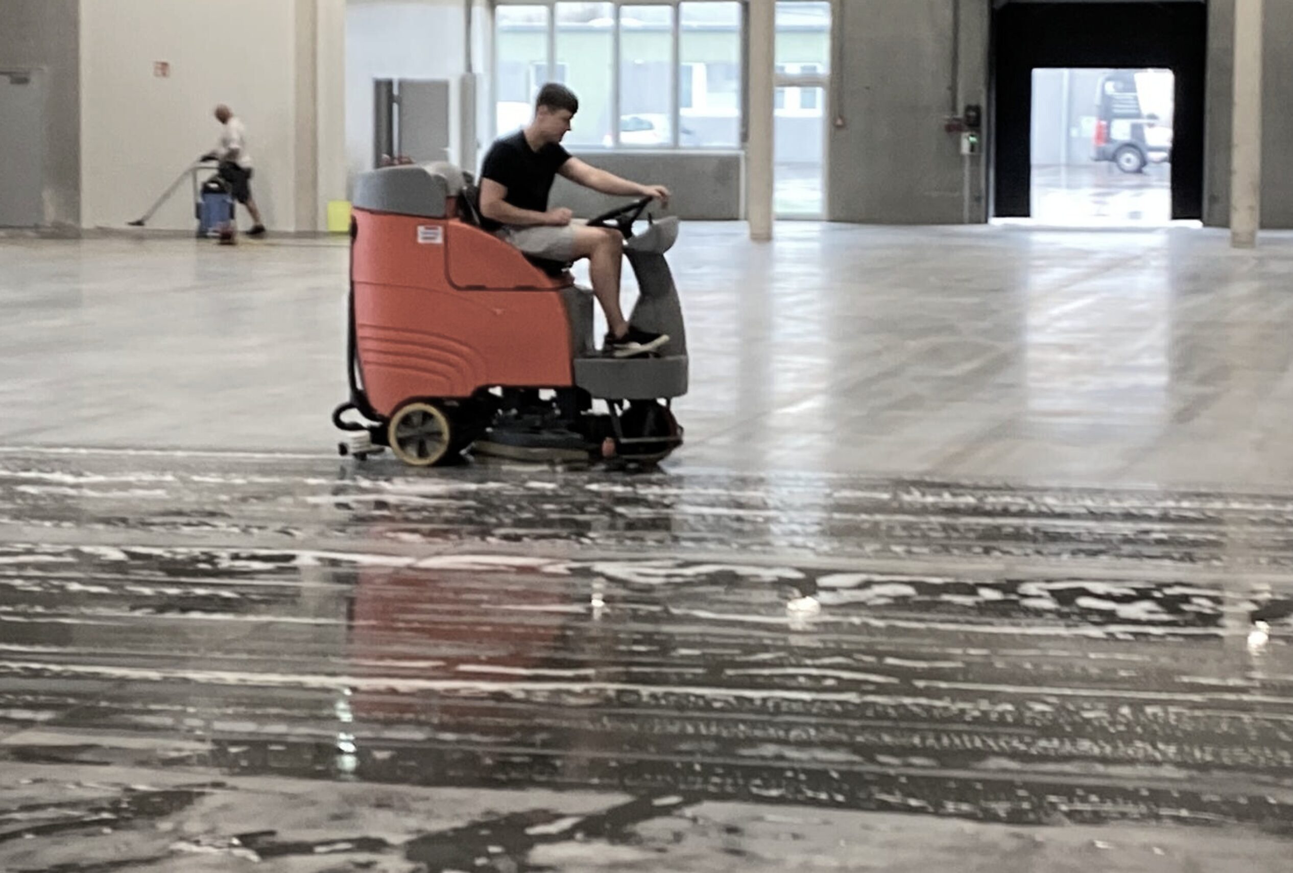 Scheuersaugmaschine reinigt großen Hallenboden mit Wasser und Reinigungsmittel.