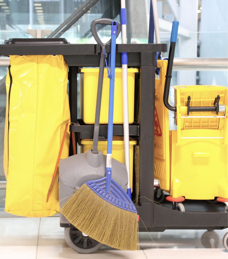 Reinigungswagen mit Besen, Mopps, Eimern und Zubehör in einem Gebäude.