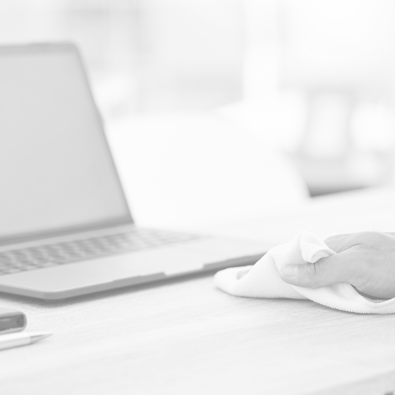Tisch wird mit einem Mikrofasertuch neben einem Laptop gereinigt.