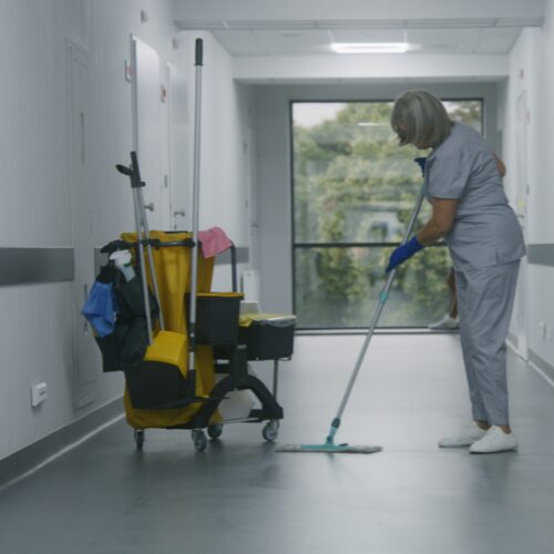 Reinigungskraft wischt den Boden in einem hellen Krankenhausflur mit professionellem Reinigungswagen – TIP-TOP Reinigung, Ordinationsreinigung Stockerau